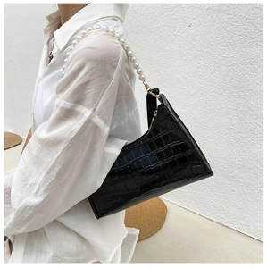 Detail of black crocodile texture bag with large pearl chain handle on white shirt