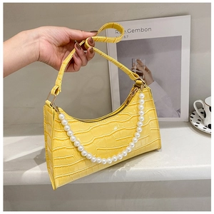 Detail of yellow crocodile pattern baguette bag with decorative faux pearl chain handle