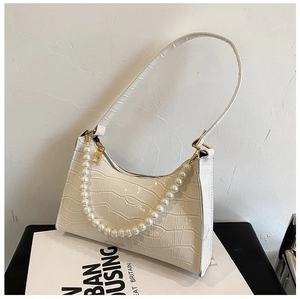 Detail of white crocodile pattern PU shoulder bag with pearl chain on a magazine
