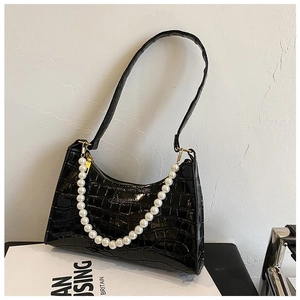 Detail of black crocodile texture baguette bag with pearl chain and leather shoulder strap