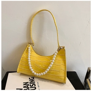 Macro shot of yellow crocodile pattern leather underarm bag with decorative pearl chain