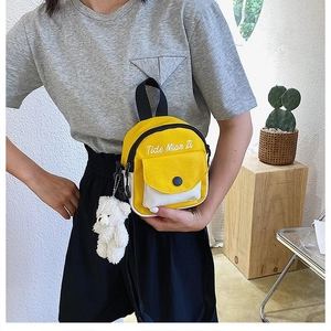 Detail of yellow and white canvas crossbody bag with teddy bear charm and embroidery