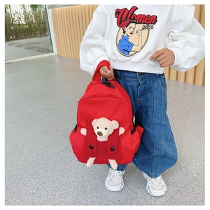 Detail view of a red kids backpack featuring a cute bear plush and decorative front pocket