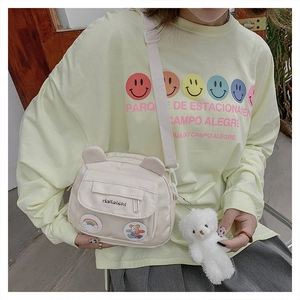 Detail of beige nylon shoulder bag featuring cute bear patches and plush keychain charm