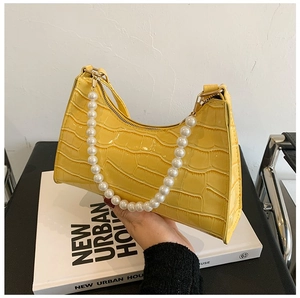 Close-up of yellow crocodile texture leather bag with white pearl handle on books