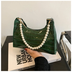 Detail of dark green crocodile texture handbag featuring a large white pearl handle