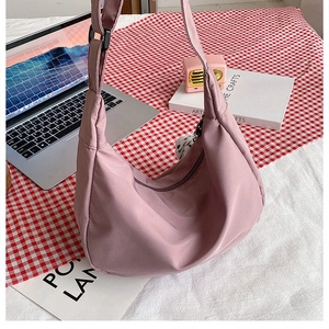 Detail of dusty pink crescent bag with nylon texture, black strap and ball pendant