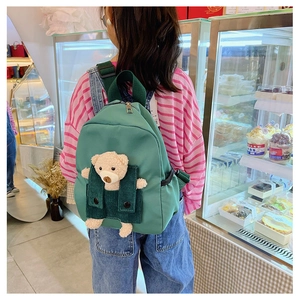 Kid carrying a green canvas backpack featuring a cute 3D plush bear decorative detail