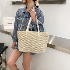 Large cream straw woven tote bag with leather handles shown in a minimalist studio setting