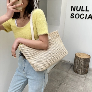 Minimalist woven straw tote bag with long leather handles shown on shoulder by model