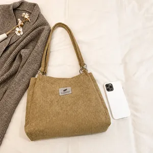 Detailed close-up of corduroy tote bag with metallic ring and decorative label patch