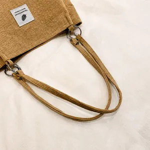 Close-up of corduroy tote bag strap with silver metal ring and decorative fabric label