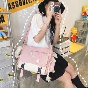 Detail of pink canvas messenger bag featuring a fuzzy white charm and adjustable strap