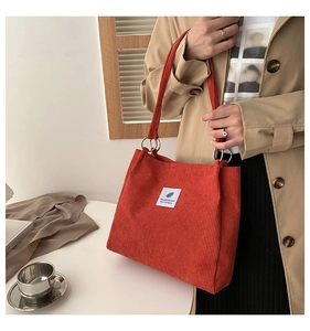 Orange corduroy tote bag detail with white feather patch on a model in beige coat