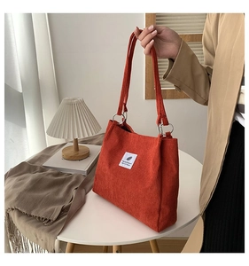 Close-up of orange corduroy tote bag detail with metal ring strap and white woven label