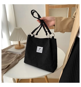 Detail of black corduroy tote bag showing silver metal ring handle attachment and label