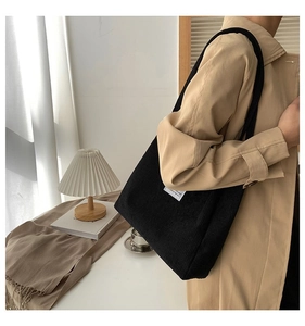 Close-up of black corduroy tote bag featuring a minimalist white rectangular woven label