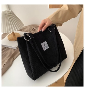 Detail of black corduroy tote bag with metal rings and minimalist white woven label