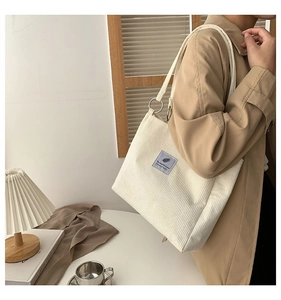 Detail of off-white corduroy tote bag worn by model in a cozy indoor setting