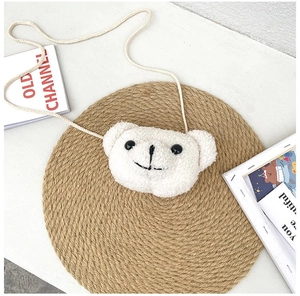 Gros plan détaillé du sac à bandoulière ours en peluche blanc sur un tapis de paille