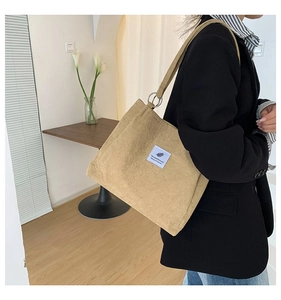 Detail of light brown corduroy tote bag showing leaf logo patch and silver metal ring strap attachment