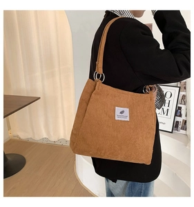 Brown corduroy tote bag with metal ring hardware and leaf patch detail shown on model