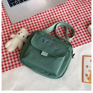 Close-up of green canvas crossbody bag featuring Dance embroidery and plush bear charm