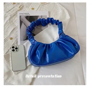 Detail view of royal blue pleated cloud bag showing compact size next to a smartphone