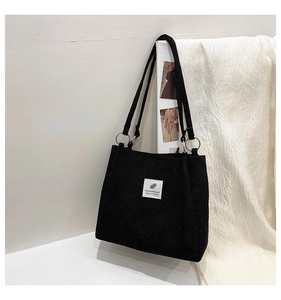 Detail of black corduroy tote bag showing silver metal rings and feather brand label