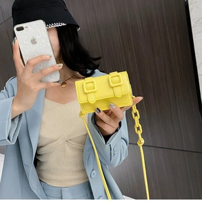 Detail of bright yellow mini crossbody bag with double decorative buckles and chain strap