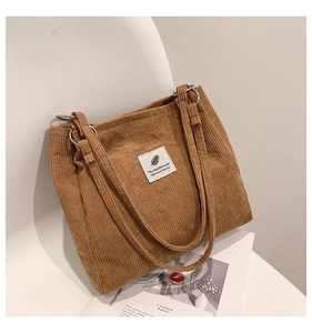 Detailed close-up of brown corduroy tote bag with white patch on a minimalist chair