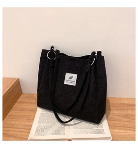 Close-up of black corduroy tote bag showing vertical rib texture and white brand label
