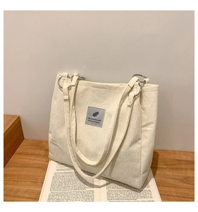 Detailed texture of white corduroy tote bag with feather patch and metallic buckle
