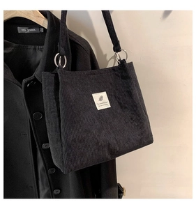 Detail of black corduroy tote bag with woven label and metal ring strap connectors