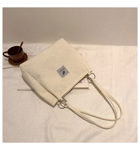 Detail of off-white corduroy tote bag showing striped texture and feather label