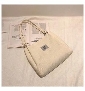 Detail of white corduroy tote bag with grey leather patch on textured fabric background