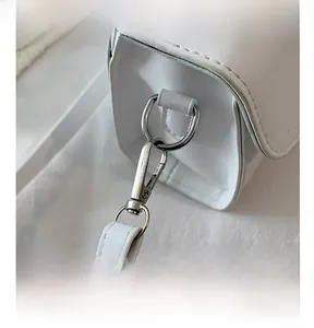 Close-up of silver metal hardware and fine stitching on white leather crossbody bag
