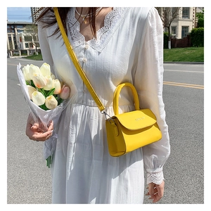Detail of a bright yellow mini handbag with flap closure and adjustable shoulder strap