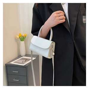 Detail of white mini crossbody bag with glossy finish held by a model in a minimal setting
