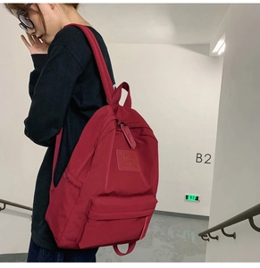Seitenansicht eines roten Nylon-Rucksacks mit Reißverschlussfach und Logo-Aufnäher