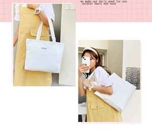 Close-up of a white canvas tote bag with letter patch detail and large capacity