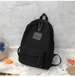 Detail eines schwarzen Nylon-Rucksacks mit vorderer Klappentasche und Leder-Logo-Patch