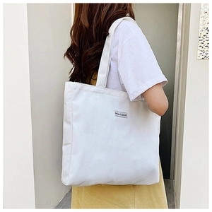 Detailed view of white canvas tote bag with 'Believe in yourself' tag on model shoulder
