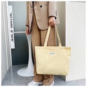 Detail of beige canvas tote bag showing wide straps and Believe in yourself woven label