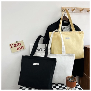 Three canvas tote bags in black, white, and yellow colors on a checkered table