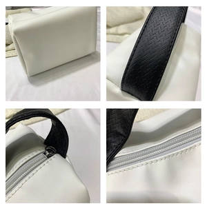 Detail view of white leather vanity bag with textured black handle and metal zipper