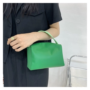 Detail view of bright green trapezoid handbag with textured leather and slim handle