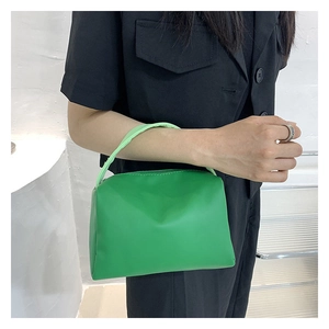 Detail showing a green rectangular leather handbag with cylindrical handle and zipper closure