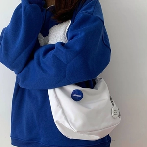 Detail view of a white nylon messenger bag featuring a blue 'FASHION' badge and a round tag
