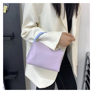 Détail d'un sac à main carré violet avec anse bleue porté avec un blazer blanc élégant